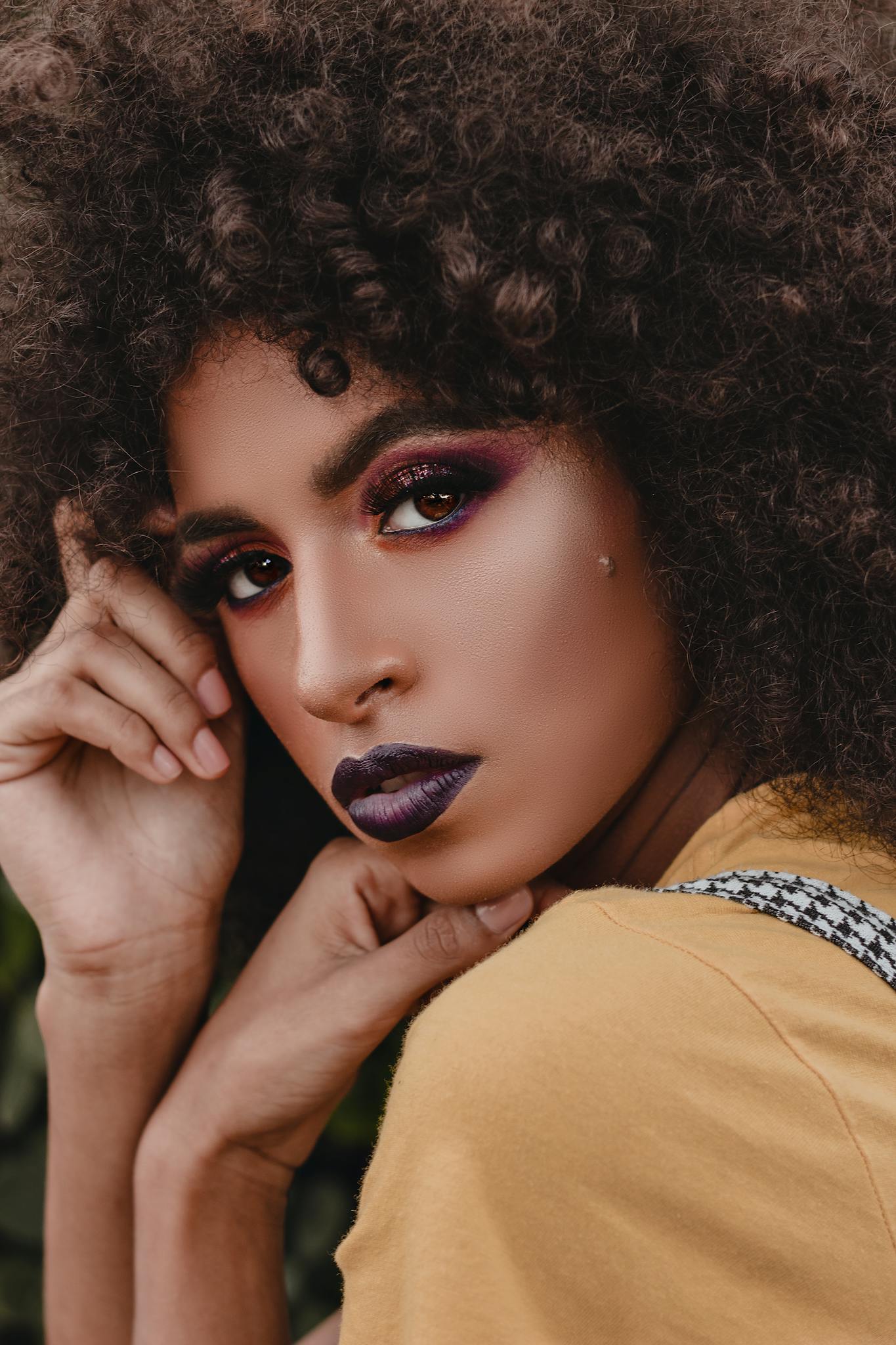 Close-up portrait of a woman showcasing bold makeup and curly hair in an artistic photoshoot.